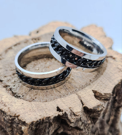 Dos Anillos tipo alianza de matrimonio o pareja en acero inoxidable con Cadena negra y ancho de 6mm. Se incluye grabado de nombres y fecha importante gratis. Posan sobre tronco.