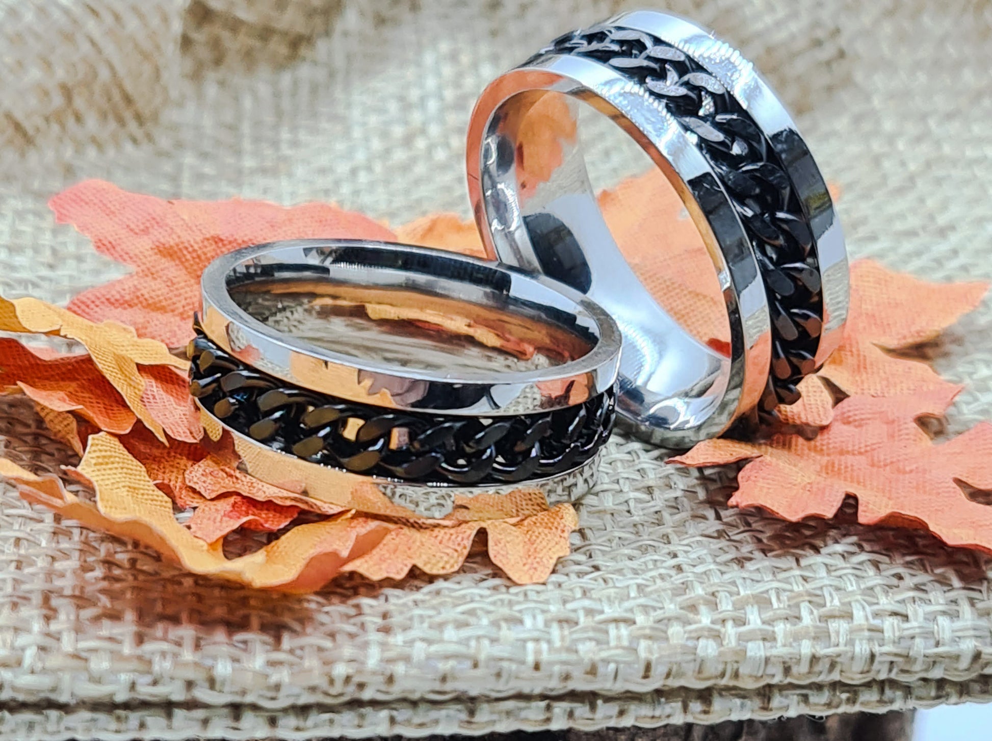 Dos Anillos tipo alianza de matrimonio o pareja en acero inoxidable con Cadena negra y ancho de 6mm. Se incluye grabado de nombres y fecha importante gratis. Posan sobre saco.