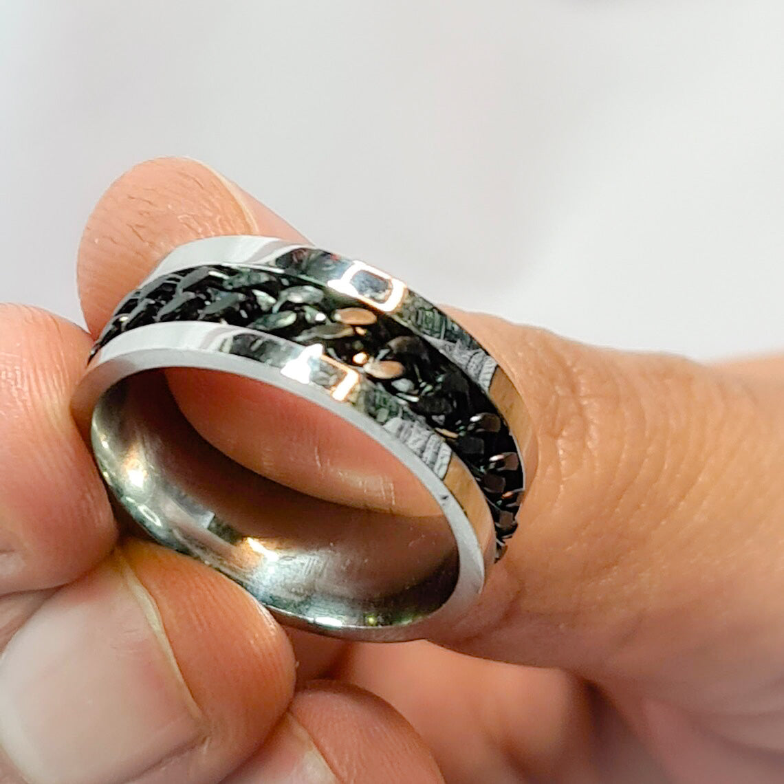 Anillo tipo alianza de matrimonio o pareja en acero inoxidable con Cadena negra y ancho de 6mm. Se incluye grabado de nombres y fecha importante gratis. Posa sobre mano de hombre.