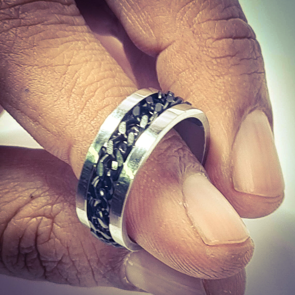Anillo tipo alianza de matrimonio o pareja en acero inoxidable con Cadena negra y ancho de 6mm. Se incluye grabado de nombres y fecha importante gratis. Posa sobre mano de hombre.
