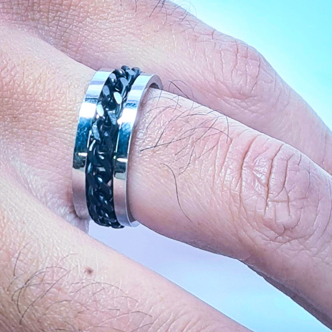 Anillo tipo alianza de matrimonio o pareja en acero inoxidable con Cadena negra y ancho de 6mm. Se incluye grabado de nombres y fecha importante gratis. Posa sobre mano de hombre.