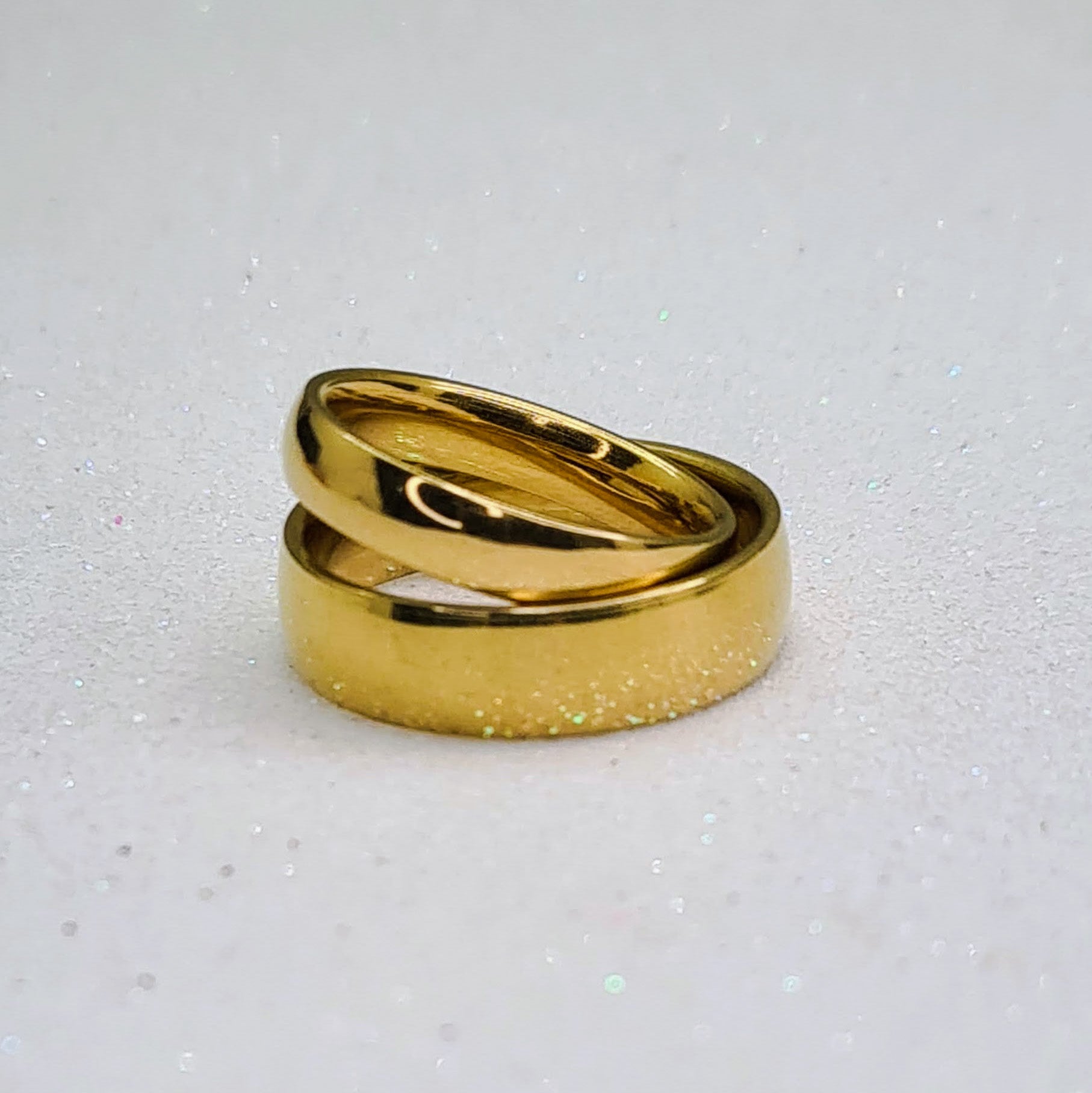 Anillos tipo alianza de matrimonio o pareja en acero inoxidable dorado y ancho de 4mm y 6mm. Se incluye grabado de nombres y fecha importante gratis. Posan sobre fondo blanco brillante.