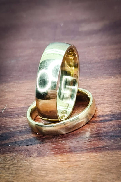 Anillos tipo alianza de matrimonio o pareja en acero inoxidable dorado y ancho de 4mm y 6mm. Se incluye grabado de nombres y fecha importante gratis. Posan sobre madera.