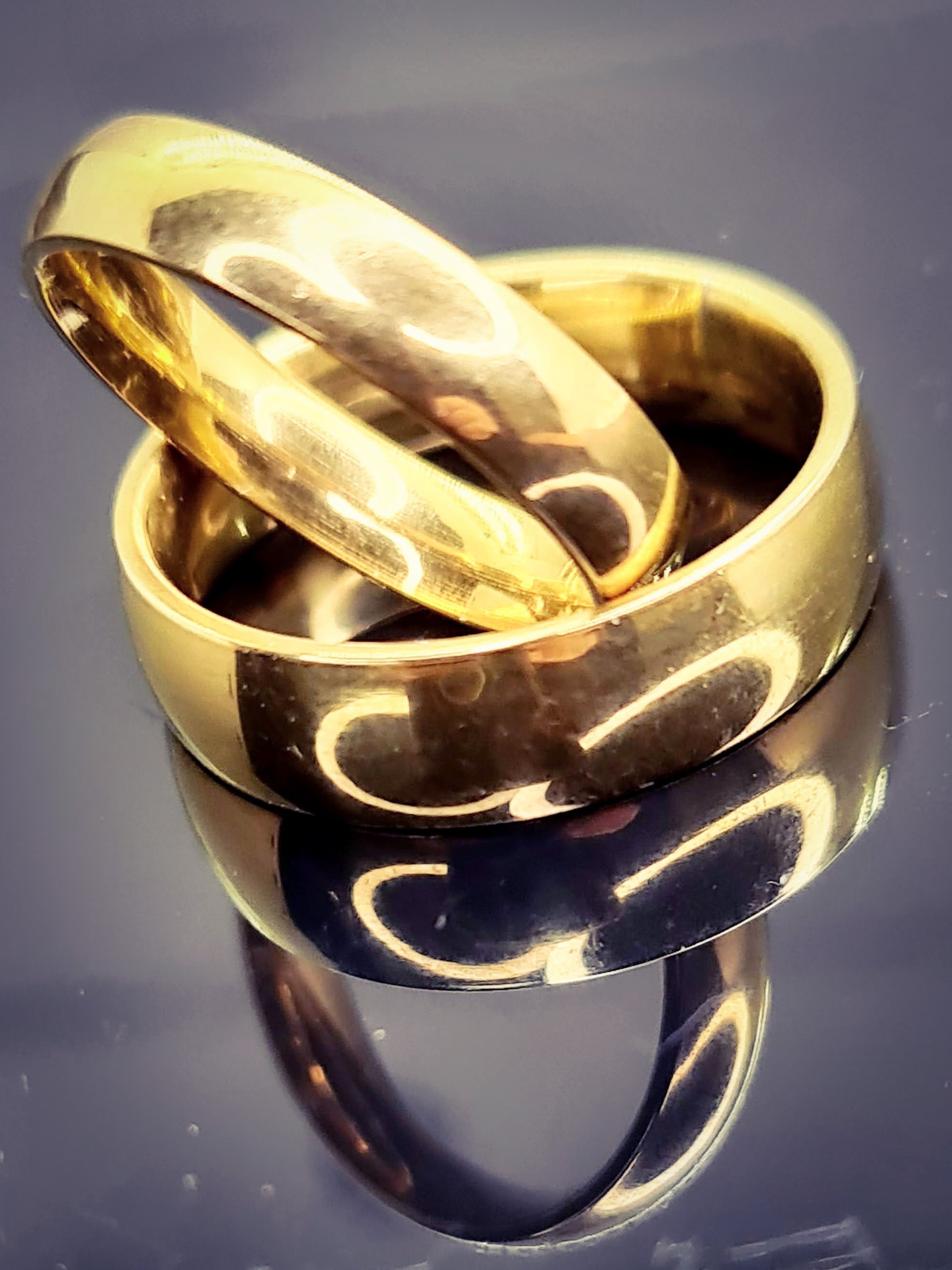 Anillos tipo alianza de matrimonio o pareja en acero inoxidable dorado y ancho de 4mm y 6mm. Se incluye grabado de nombres y fecha importante gratis. Posan sobre base negra brillante.