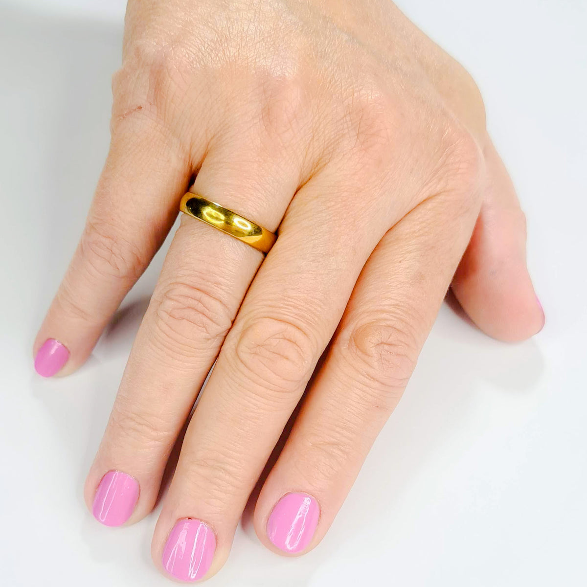 Alianza dorada unisex de 4 mm puesta en una mano femenina.