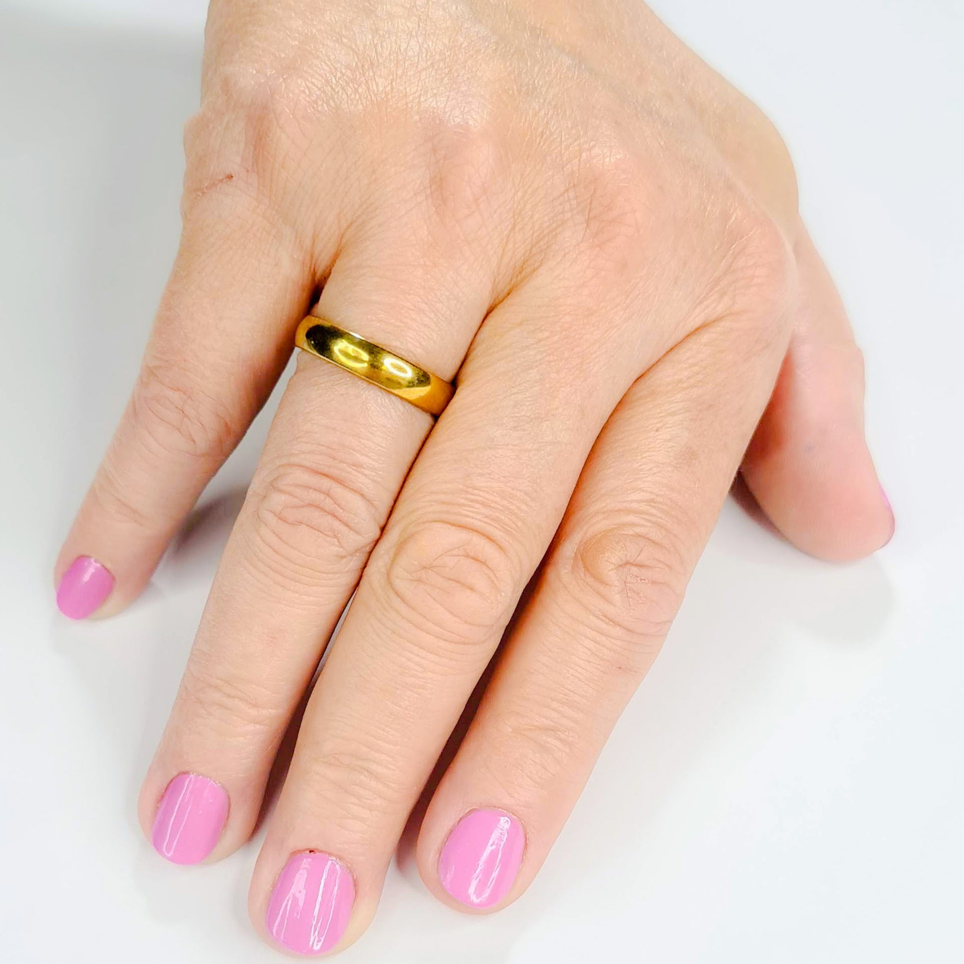 Alianza dorada unisex de 4 mm puesta en una mano femenina.