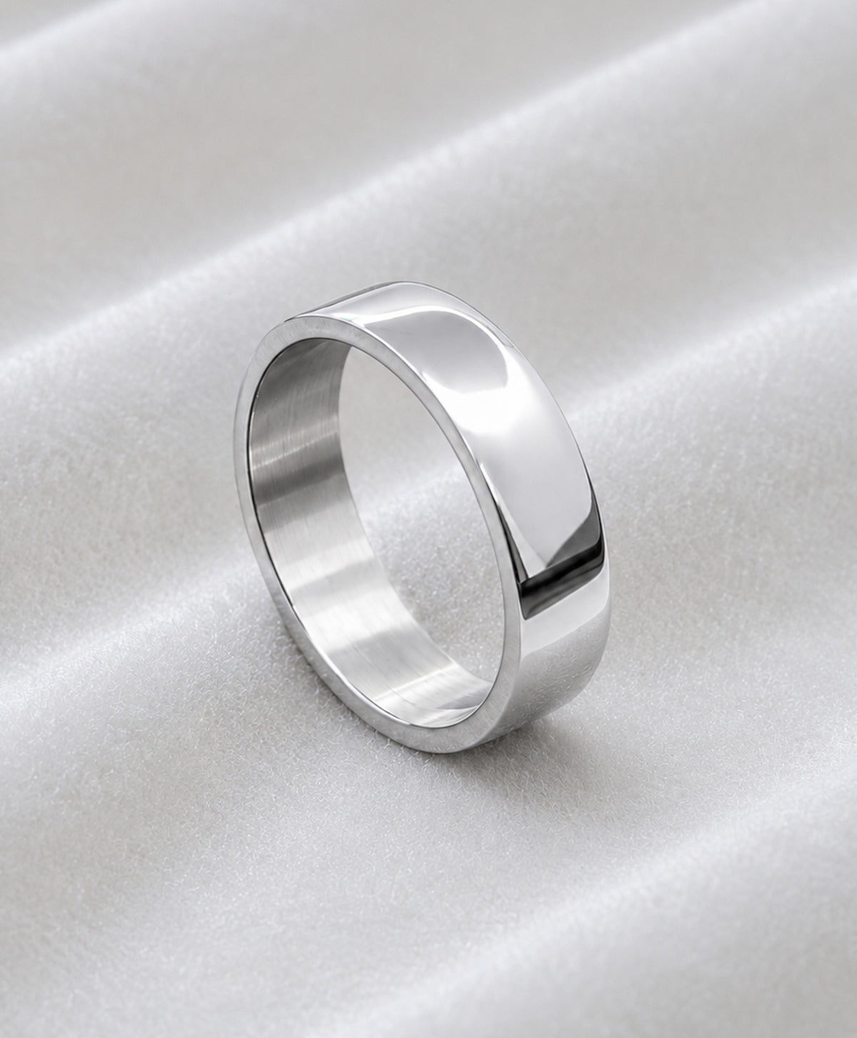 Anillo plano plateado de acero inoxidable sobre tela blanca satinada.