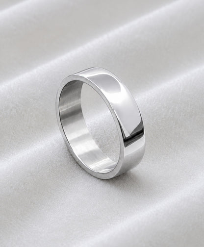 Anillo plano plateado de acero inoxidable sobre tela blanca satinada.