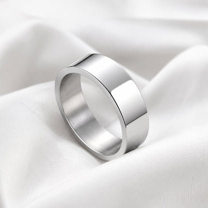 Anillo plano plateado de acero inoxidable sobre tela blanca satinada.