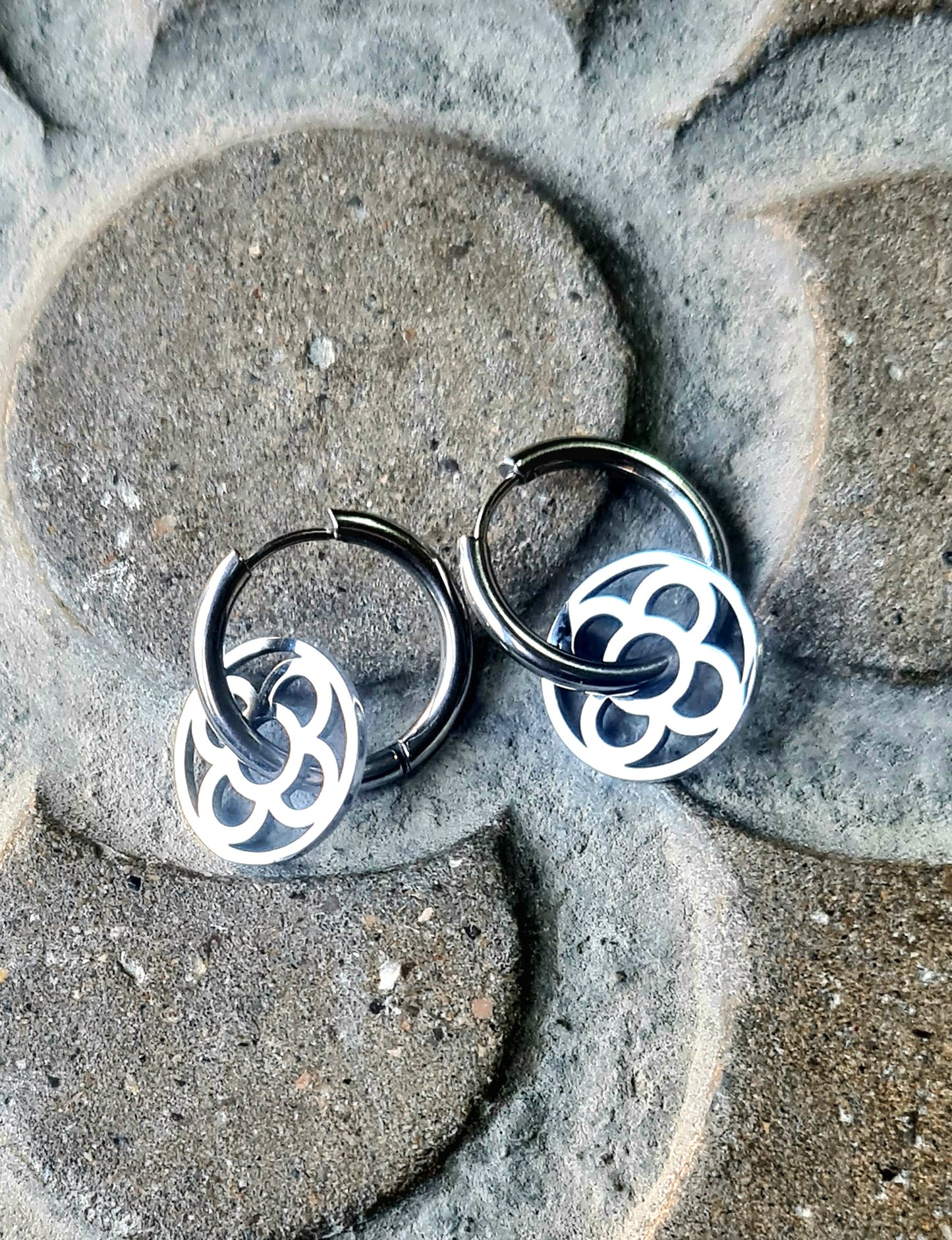 Aros con la Flor de Barcelona de acero inoxidable circular para mujer. Sobre baldosa Flor de Barcelona.