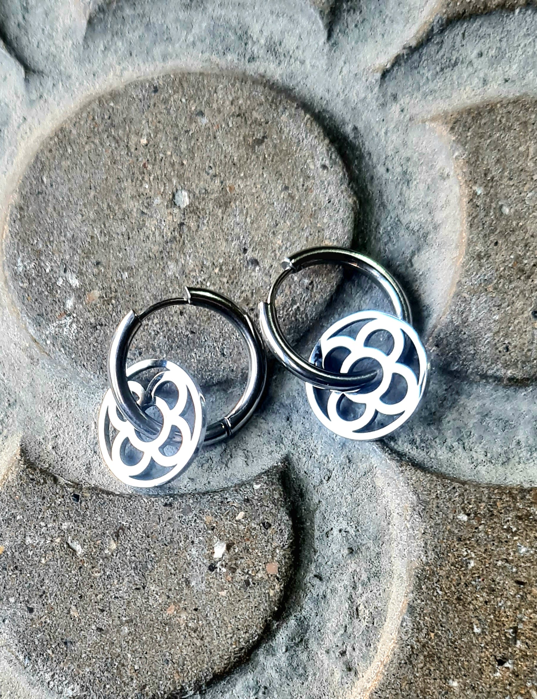 Aros con la Flor de Barcelona de acero inoxidable circular para mujer. Sobre baldosa Flor de Barcelona.