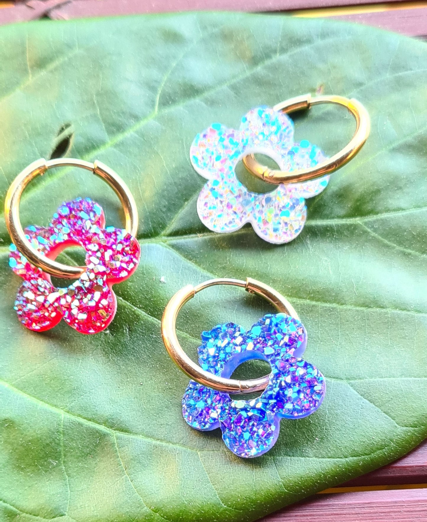 Aros acero inoxidable dorados con Flor de Acrílico Brillante para mujer. Fondo hoja verde.