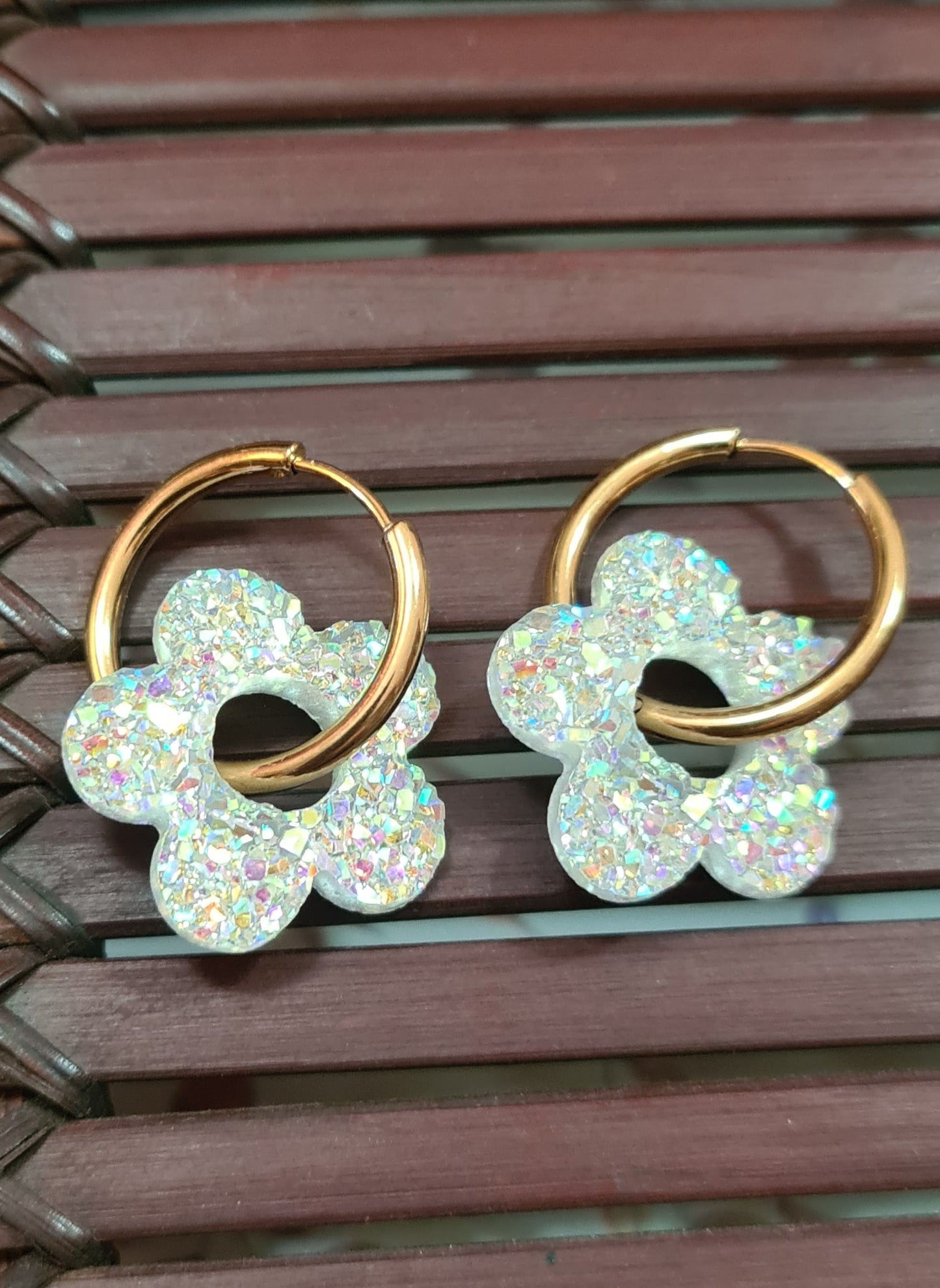 Aros acero inoxidable dorados con Flor de Acrílico Brillante para mujer. Fondo rejilla de Madera.