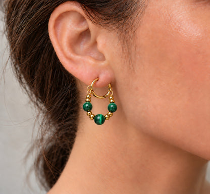 Pendiente de aro dorado con cuentas de malaquita verde llevado en la oreja.