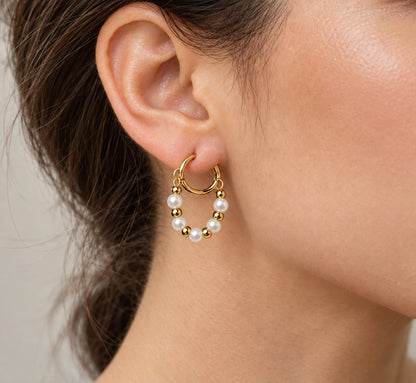 Pendiente de aro dorado con perlas blancas y detalles dorados llevado en la oreja.