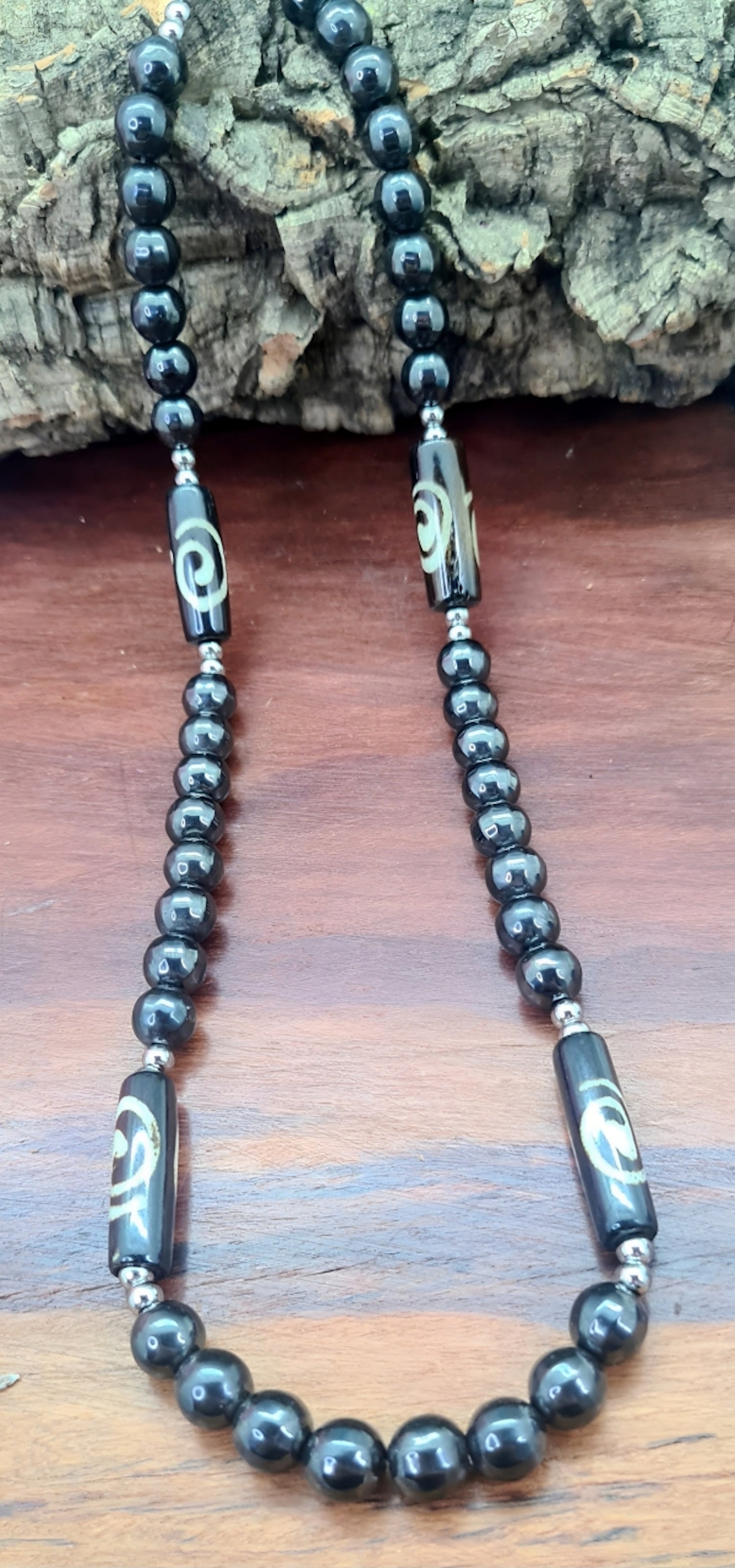 Collar para hombres cuentas de Hematite, acero y Hueso de Yak. Posa sobre madera.