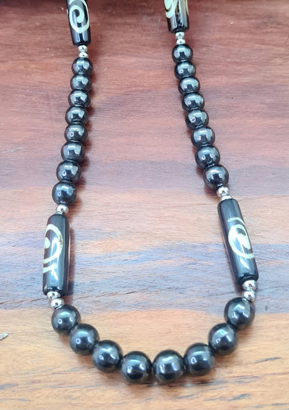 Collar para hombres cuentas de Hematite, acero y Hueso de Yak. Posa sobre madera.