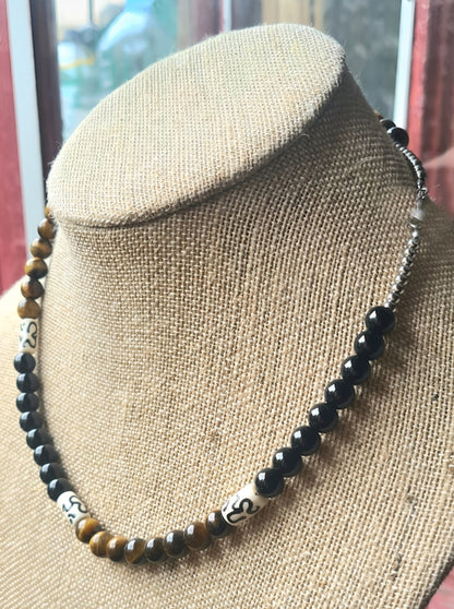 Collar de ojo de tigre y ónix expuesto sobre busto de joyería.