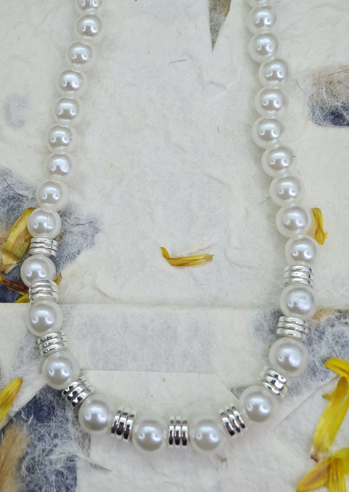 Collar de perlas y discos plateados visto puesto sobre papel decorado.