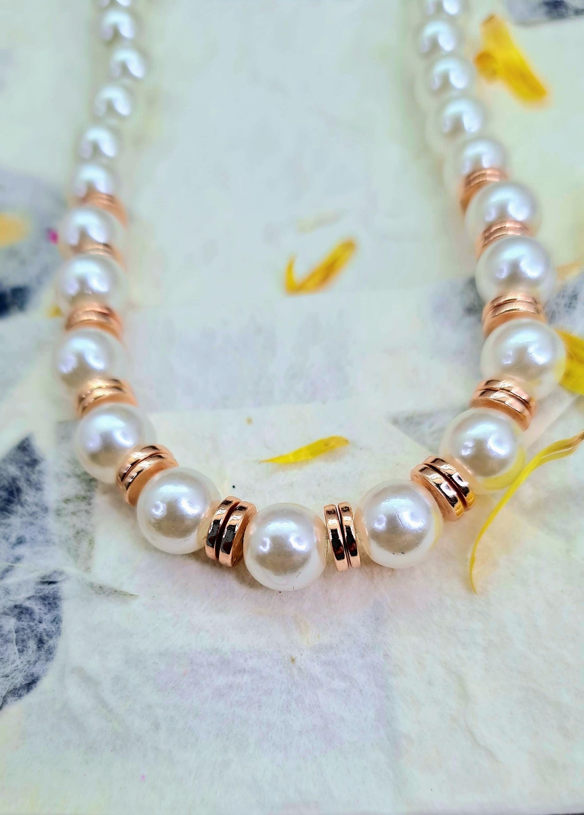Collar de perlas blancas con detalles metálicos color oro rosado puesto sobre papel decorado.