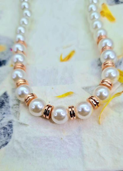 Collar de perlas blancas con detalles metálicos color oro rosado puesto sobre papel decorado.