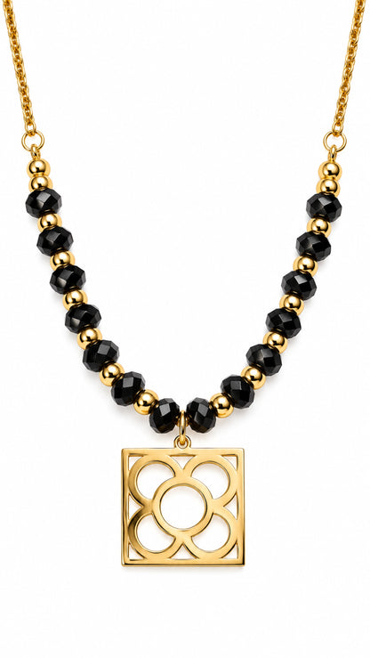 Collar Flor de Barcelona dorado con cuentas de ónix negro facetado sobre fondo blanco.