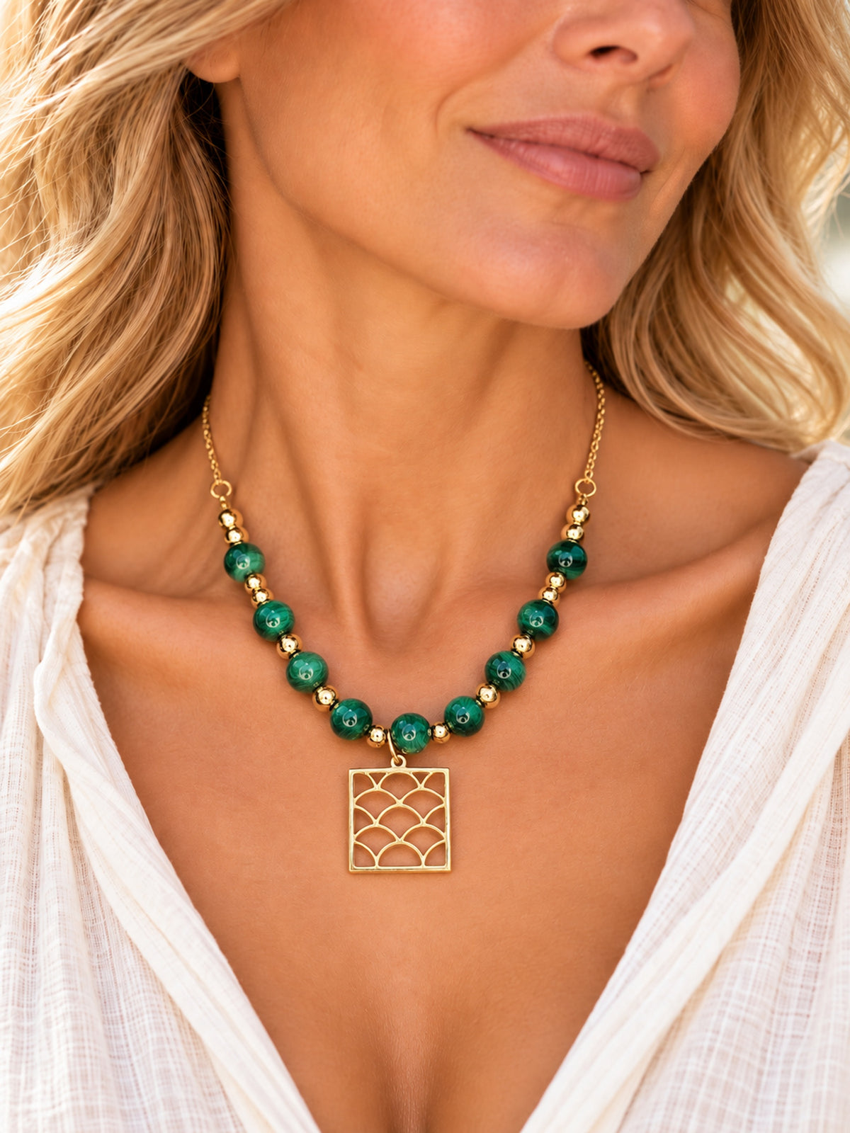 Collar de malaquita con colgante dorado de ondas llevado por una mujer.