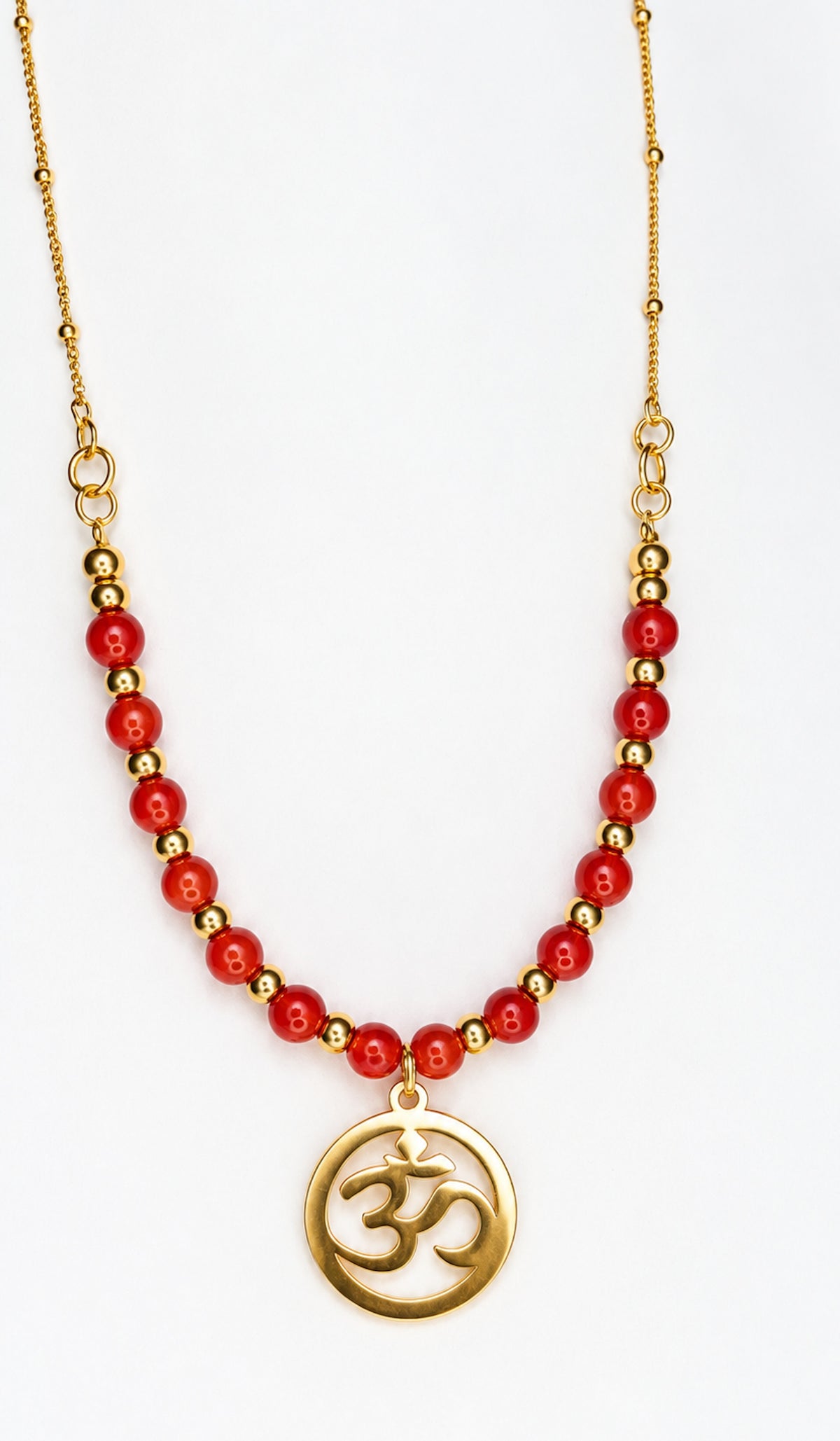 Collar dorado con cuentas de coral manzana rojo y colgante redondo con símbolo Om sobre fondo blanco.
