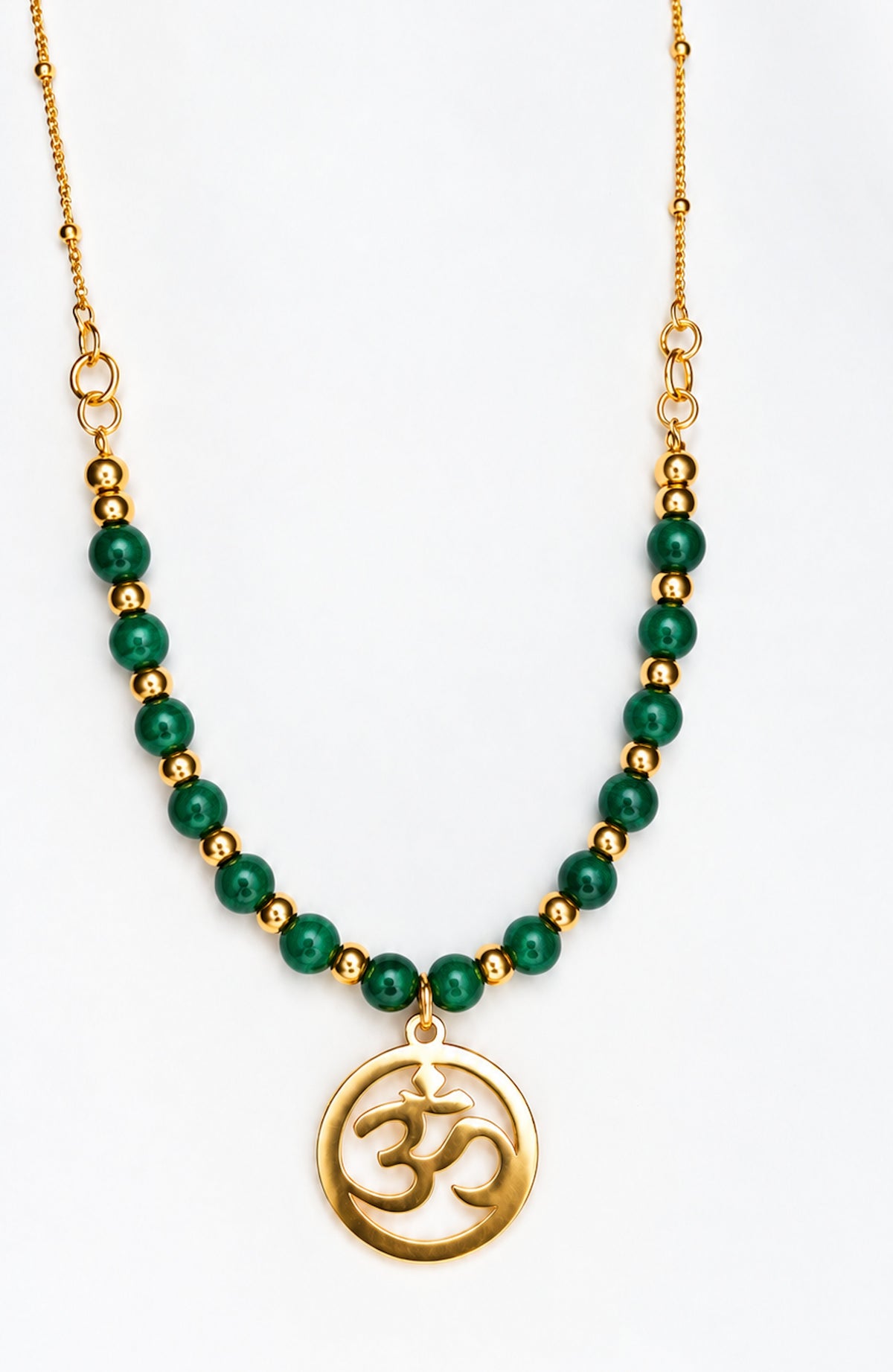 Collar dorado con cuentas de malaquita verde y colgante redondo con símbolo Om sobre fondo blanco.