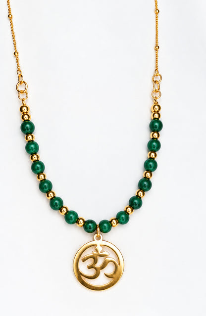 Collar dorado con cuentas de malaquita verde y colgante redondo con símbolo Om sobre fondo blanco.