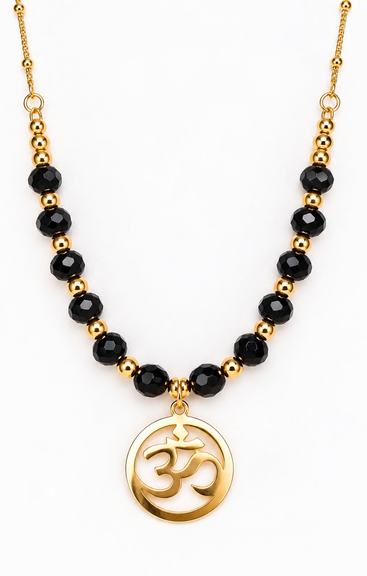 Collar dorado con cuentas de ónix negro y colgante redondo con símbolo Om sobre fondo blanco.