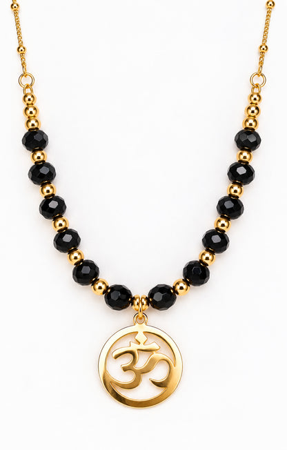 Collar dorado con cuentas de ónix negro y colgante redondo con símbolo Om sobre fondo blanco.