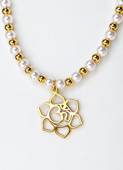 Collar dorado con perlas blancas y colgante Om dentro de una flor de loto sobre fondo blanco.
