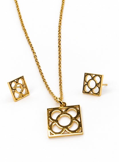 Conjunto dorado Flor de Barcelona con colgante cuadrado calado y pendientes de tope a juego sobre fondo blanco.