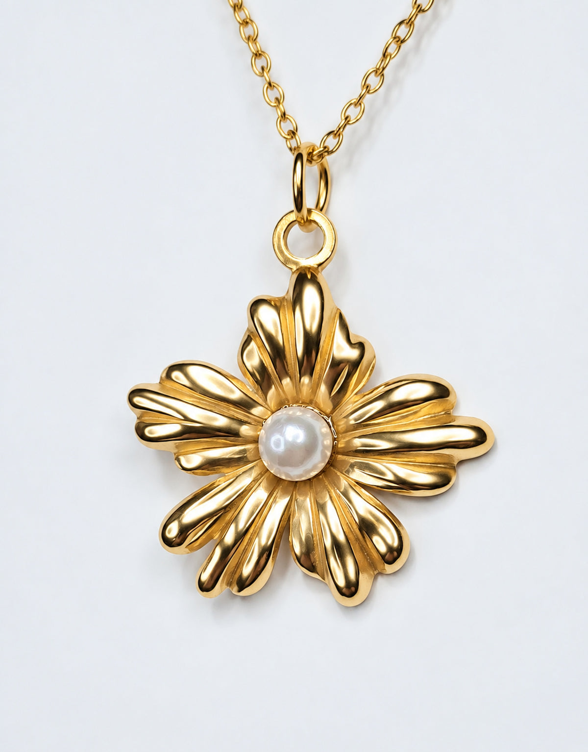 Colgante floral de acero dorado con perla central y cadena dorada sobre fondo claro.