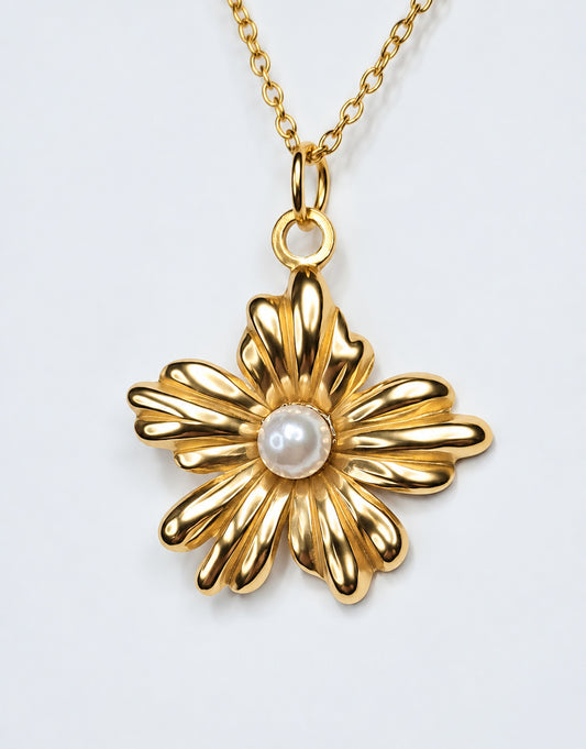 Colgante floral de acero dorado con perla central y cadena dorada sobre fondo claro.