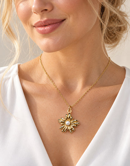 Colgante floral dorado con perla llevado al cuello con una blusa blanca.
