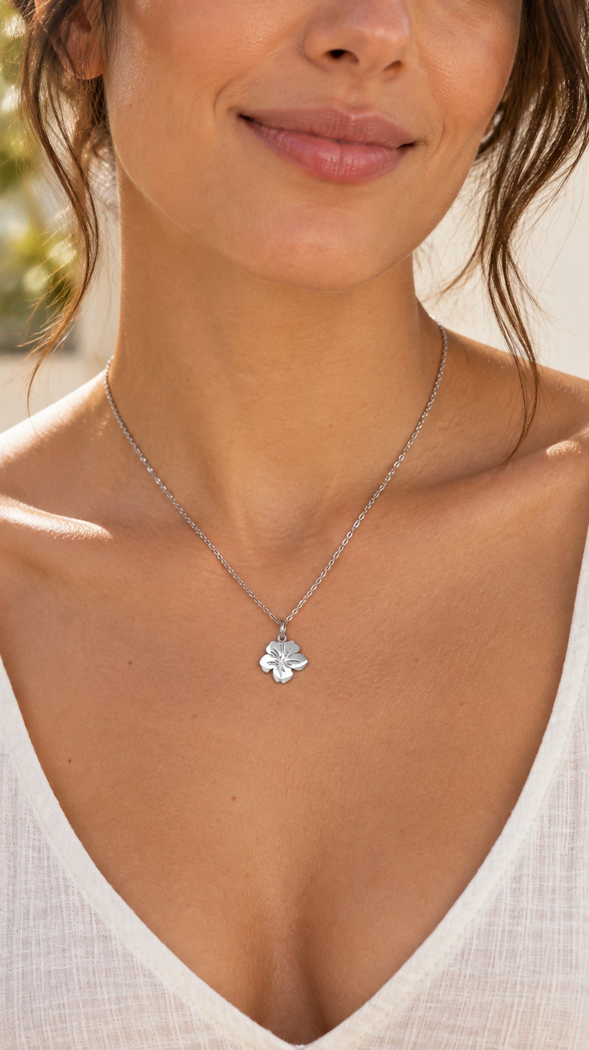 Colgante floral plateado de acero inoxidable llevado al cuello por una mujer.
