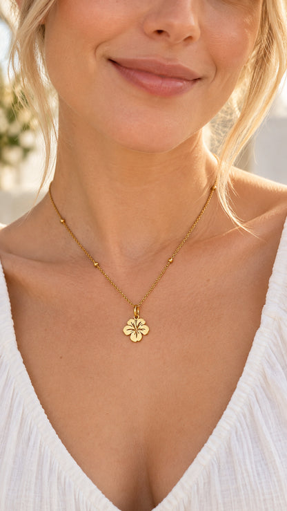 Colgante floral dorado de acero inoxidable llevado al cuello por una mujer.
