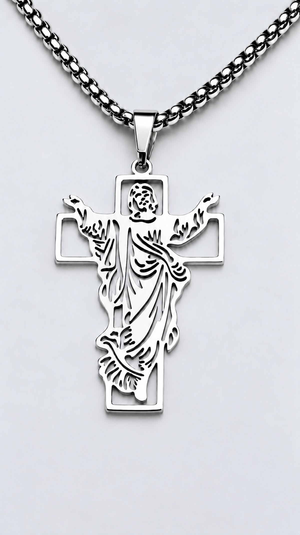 Cruz con Jesús de acero inoxidable en acabado plateado y cadena sobre fondo claro.