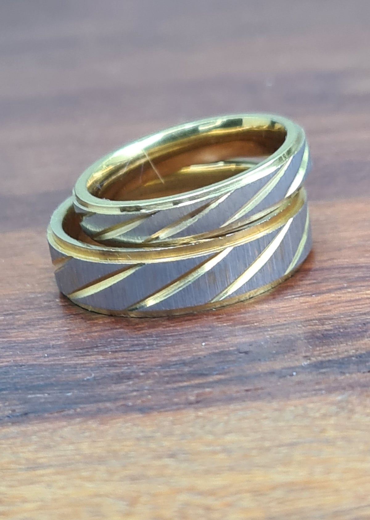 Detalle de dos anillos de acero inoxidable con centro plateado texturizado y líneas doradas.
