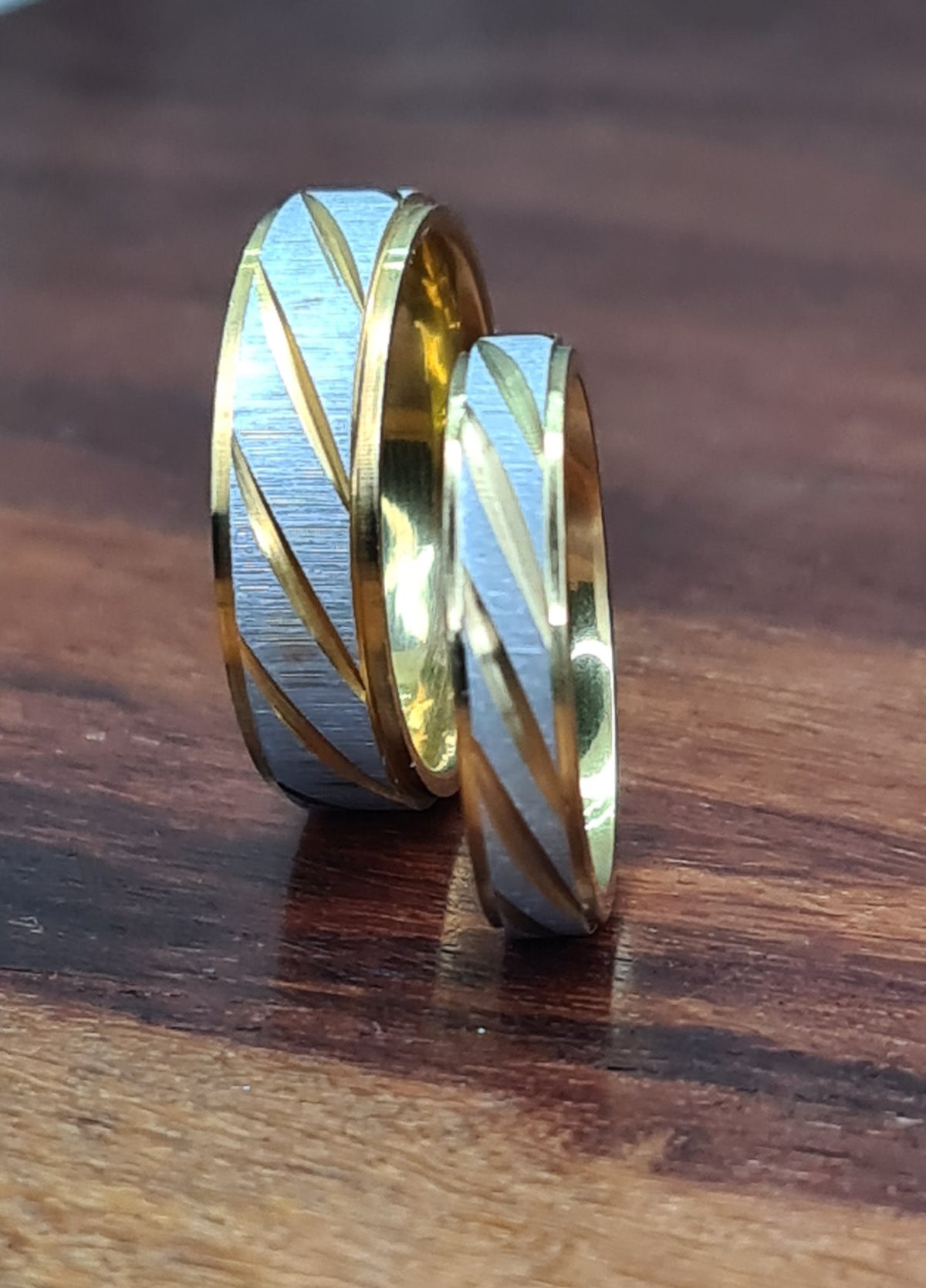 Alianzas de pareja bicolor de diferentes anchos colocadas sobre superficie de madera.