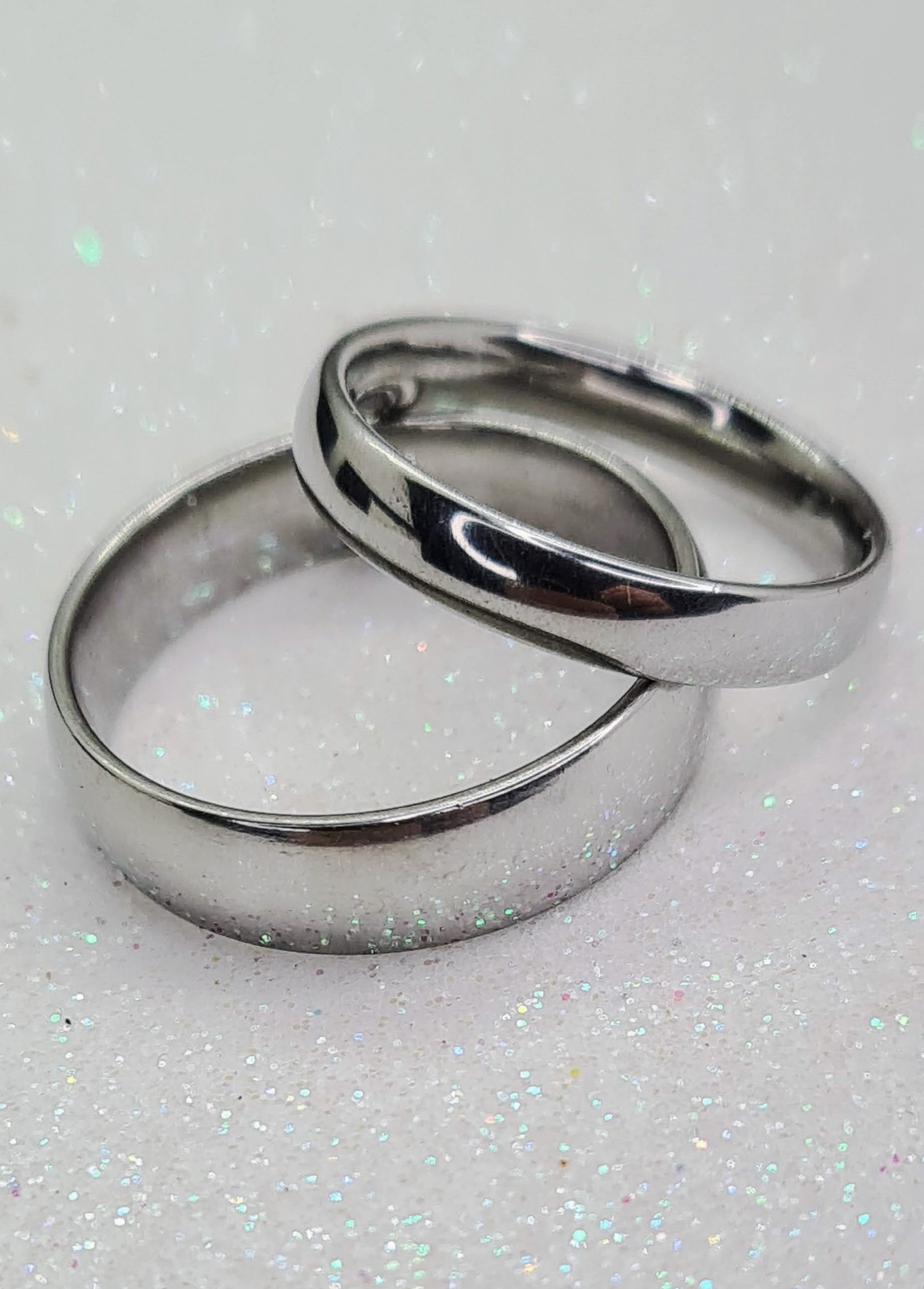 Dos Anillos tipo alianza de matrimonio o pareja en acero inoxidable media caña anchos de 4 y 6mm. Se incluye grabado de nombres y fecha importante gratis. Se posan sobre blanco.