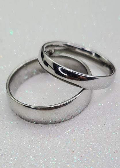 Dos Anillos tipo alianza de matrimonio o pareja en acero inoxidable media caña anchos de 4 y 6mm. Se incluye grabado de nombres y fecha importante gratis. Se posan sobre blanco.