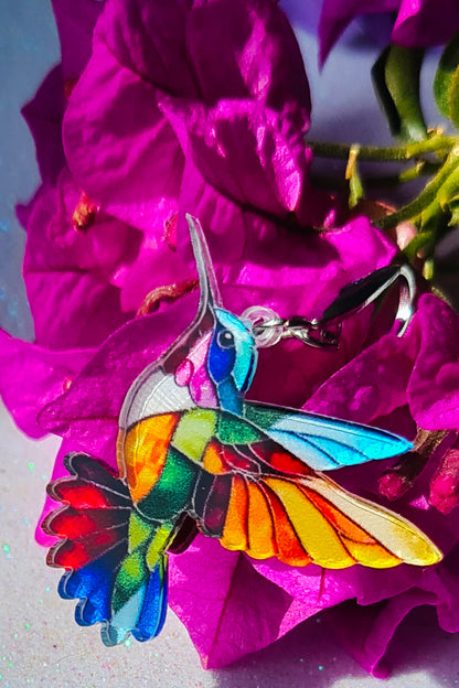 Pendientes Colibrí para mujer en Acero y Acrílico. Posa sobre fondo blanco y flores.