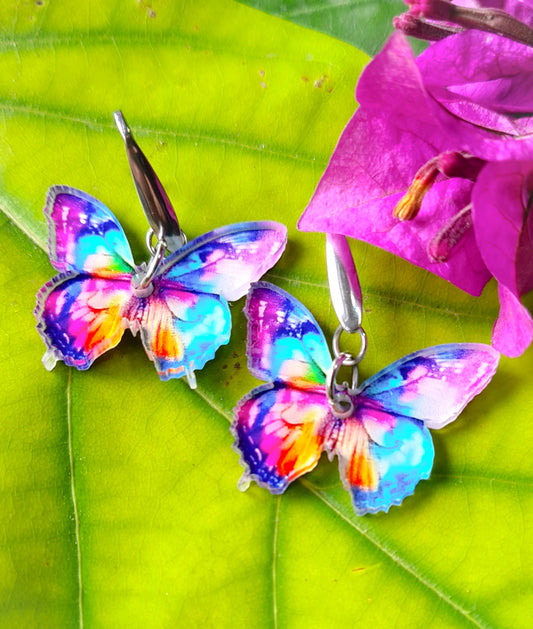 Pendientes Mariposa multicolor para mujer en Acero y Acrílico. Posa sobre hoja verde y flor.