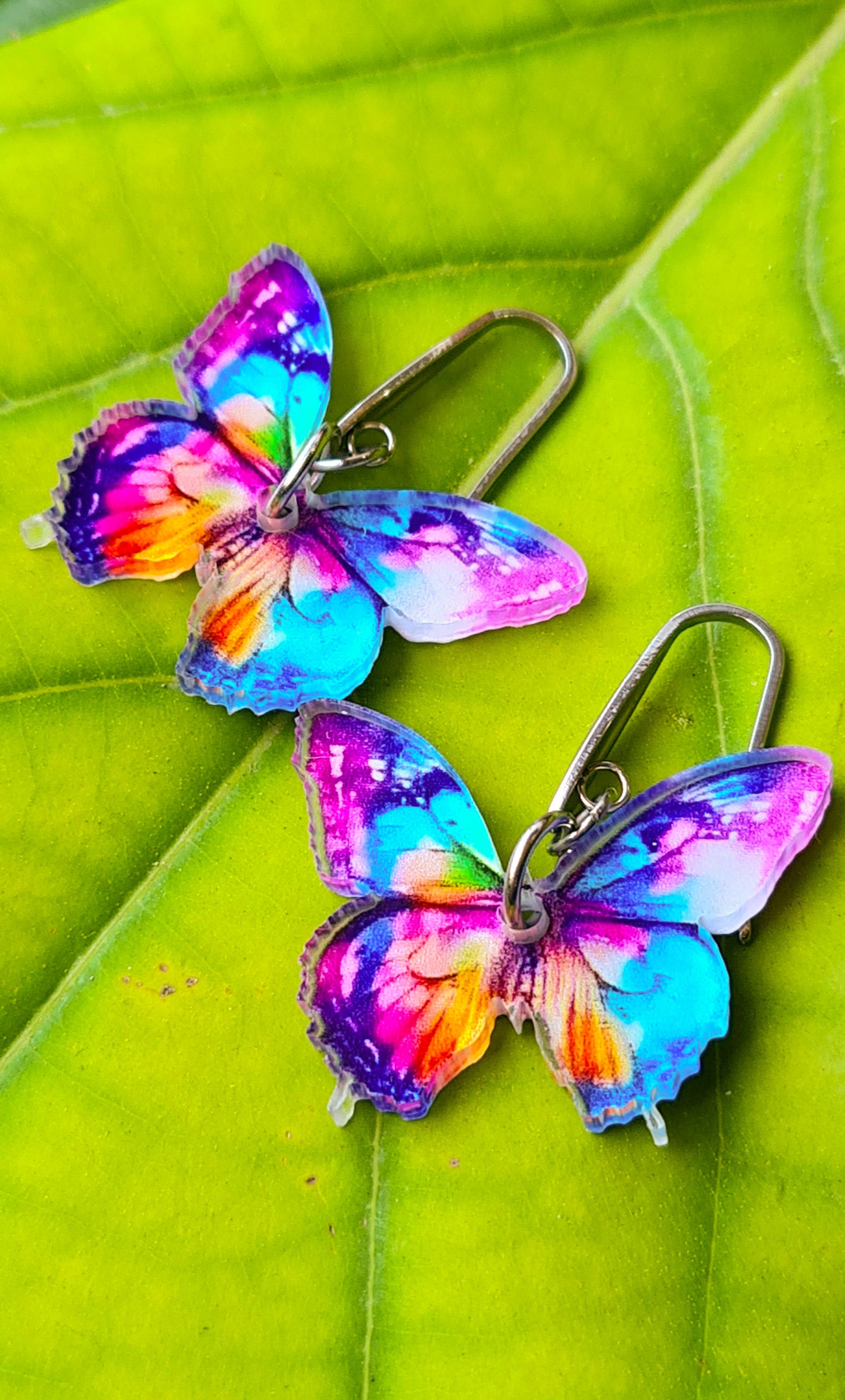 Pendientes Mariposa multicolor para mujer en Acero y Acrílico. Posa sobre hoja verde.