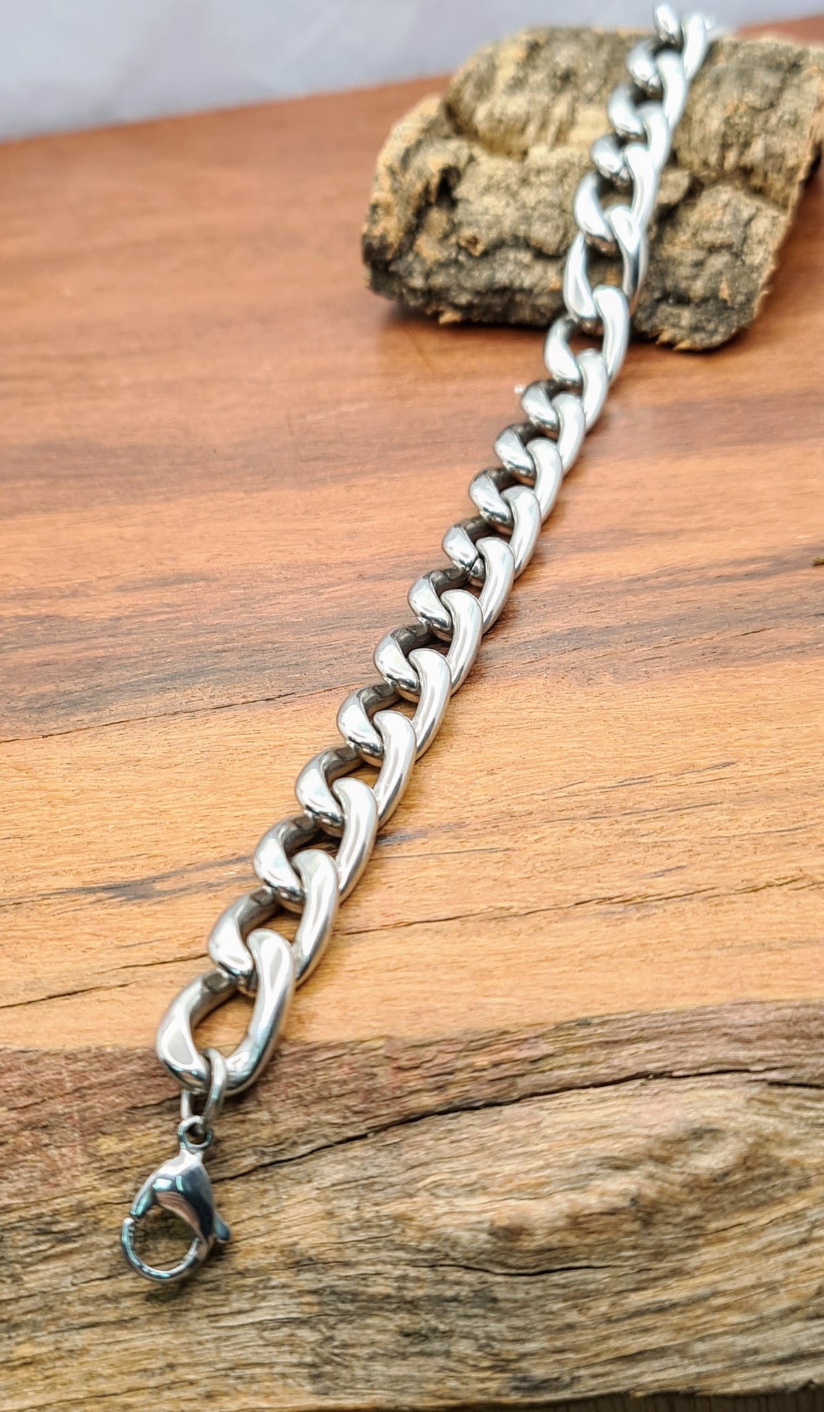 Detalle en perspectiva de pulsera masculina de eslabones de acero inoxidable sobre madera.