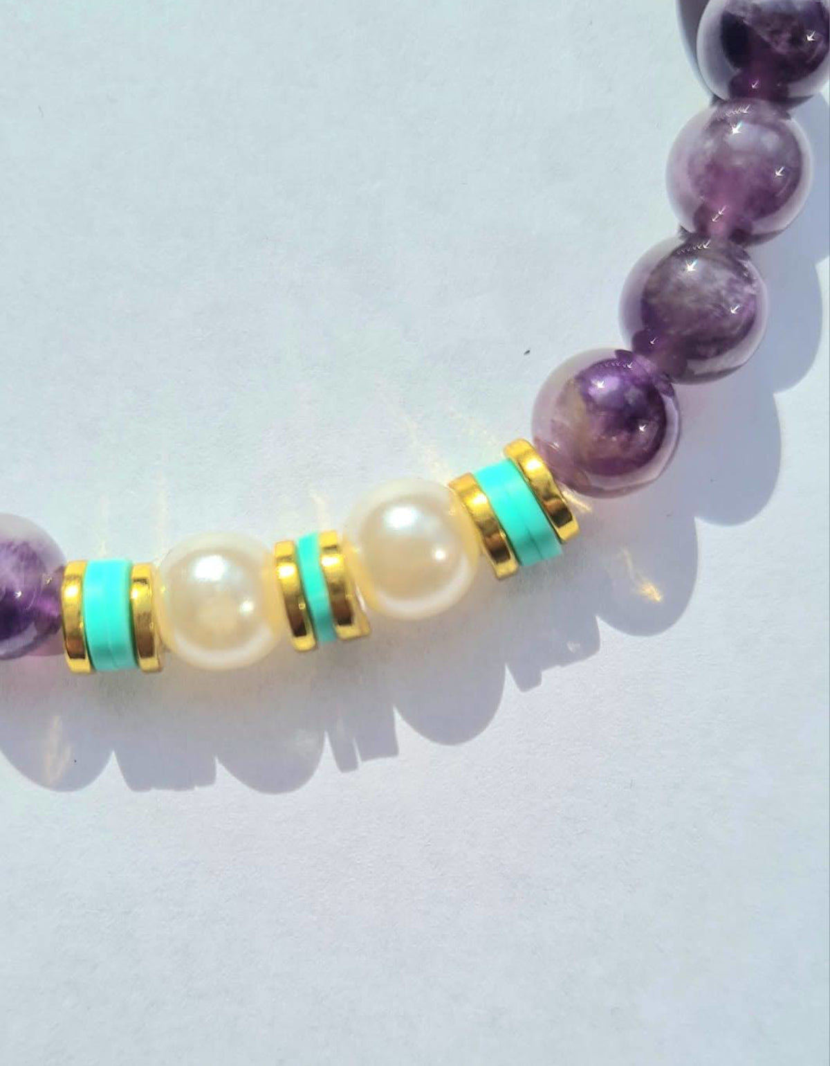 Pulsera de amatista y perlas con cerámica verde llevada en la muñeca de una mujer.