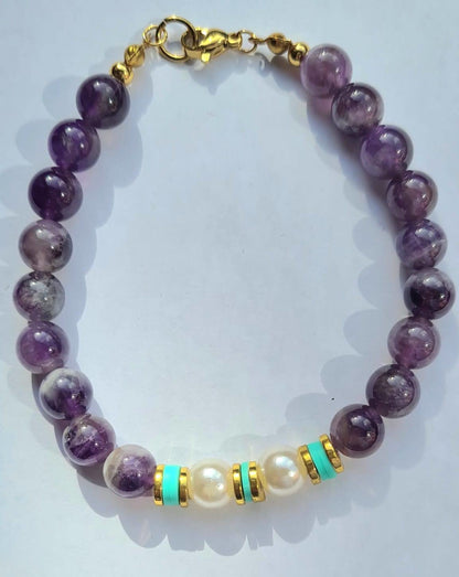 Vista completa de pulsera de amatista con perlas y detalles verdes y dorados, cierre y extensión visibles.